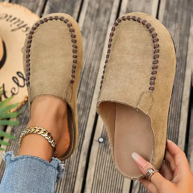 Lysebrune slip-on sandaler set ovenfra, den ene på foden og den anden holdt op, så indersålen og syningen ved tåen ses. 2