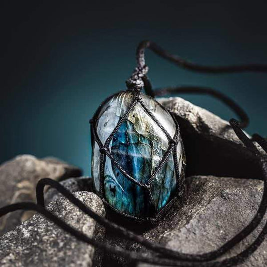 Labradorit-Anhänger mit schwarzem Band, Edelstein-Schmuck, blau-grün, auf Felsen liegend.