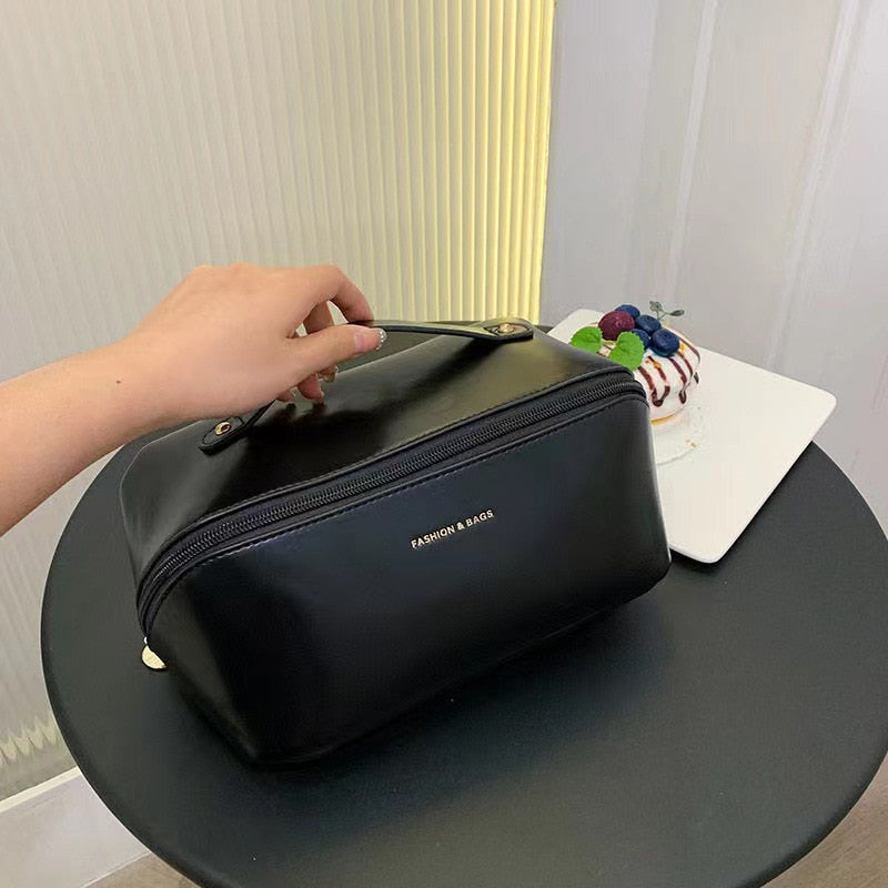 Schwarze Kosmetiktasche aus Leder mit Reißverschluss auf rundem Tisch, Hand hält Griff.