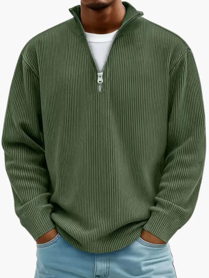 Model i mørkegrøn ribstrikket trøje med kvart lynlås og høj krave, hvid T-shirt under og lyseblå jeans. 8