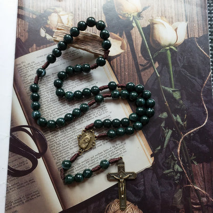 Rosenkranz mit grünen Perlen und Kreuz auf Buch und Rosenhintergrund, religiöses Schmuckstück.