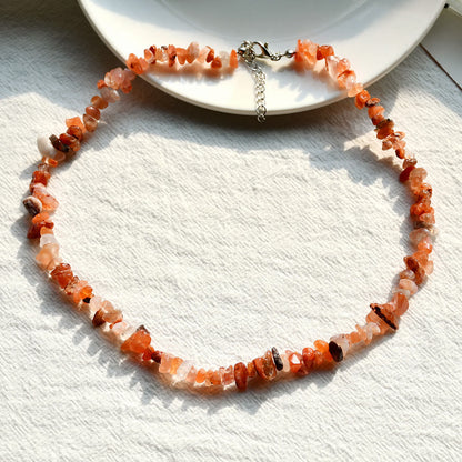 Halskette aus orangefarbenen Edelsteinen auf weißem Hintergrund, handgefertigter Schmuck.