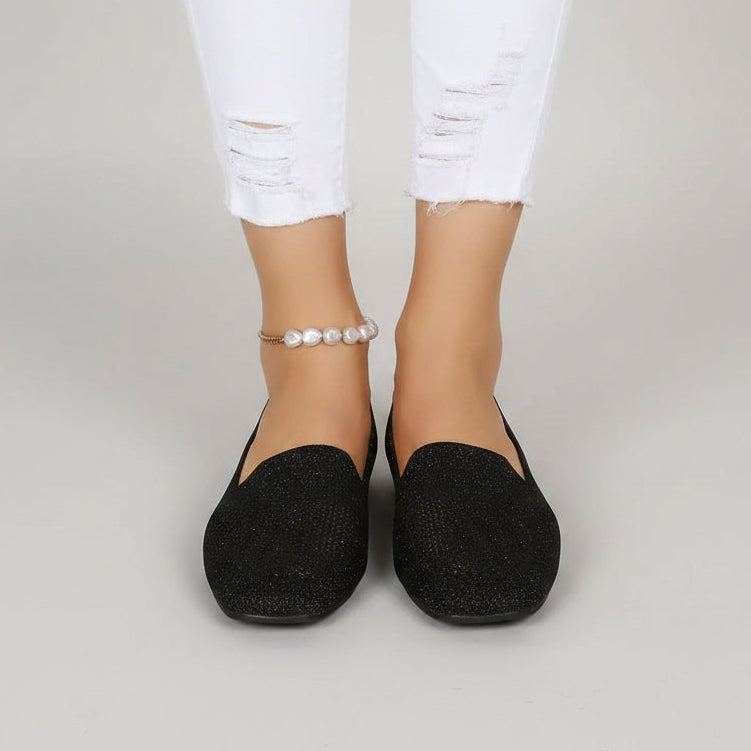 Sorte slip-on sko med firkantet tå set forfra på en model i hvide flossede jeans og perleanklet. 2