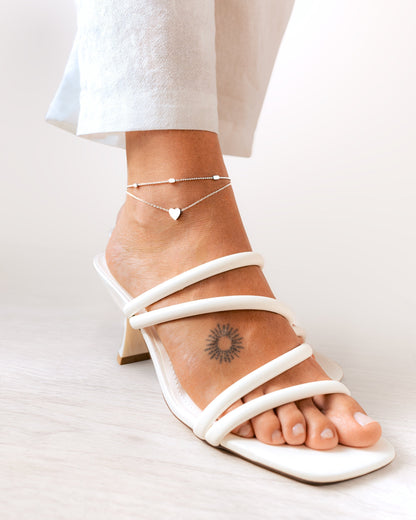 Weiße Sandalette mit Absatz, Fußkettchen mit Herzanhänger, Tattoo am Knöchel, Damenmode.