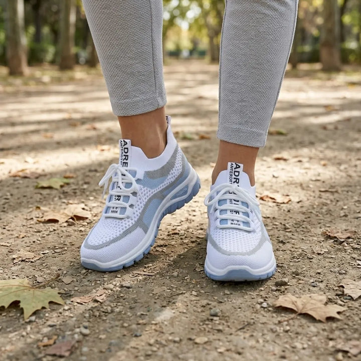 Hvide sneakers med blå sål båret af en kvinde i grå leggings på en sti med efterårsblade. 2