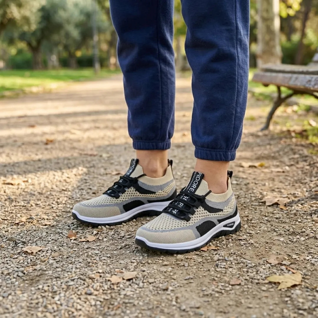 Person i marineblå joggingbukser står på en grusset sti i en park i beige sneakers med sorte detaljer og sort sål. 38