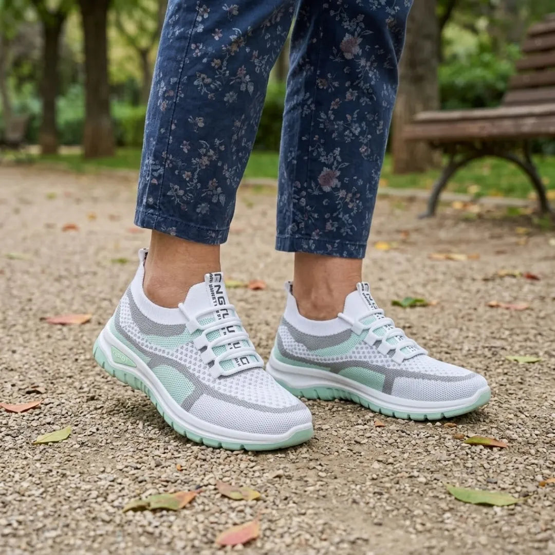 Hvide sneakers med mintgrøn sål båret af en kvinde i blomstrede bukser på en grussti i en park. 11