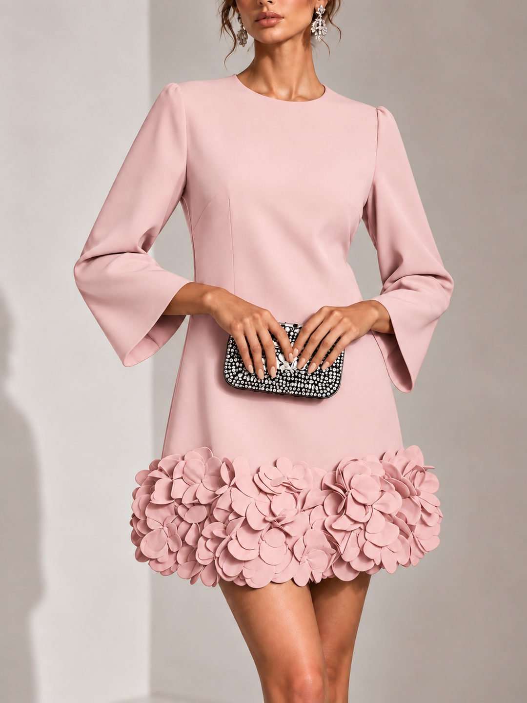 Lyserød kort kjole set forfra på model med glitrende clutch og 3D-blomsterapplikation langs kanten. 9