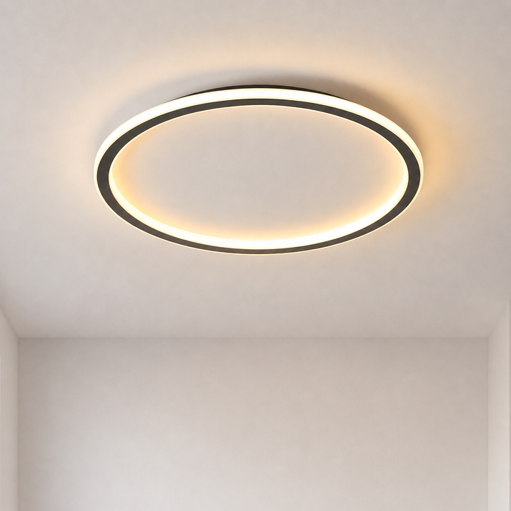 Tændt sort ringformet loftlampe set nedefra på et hvidt loft med varmt, blødt lys i hjørnet af et rum. 1