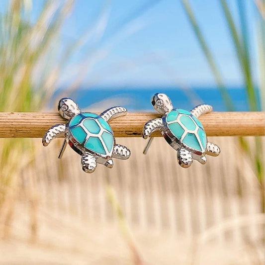 Schildkröten-Ohrringe aus Silber und Türkis, Strandhintergrund, Modeschmuck Accessoire.