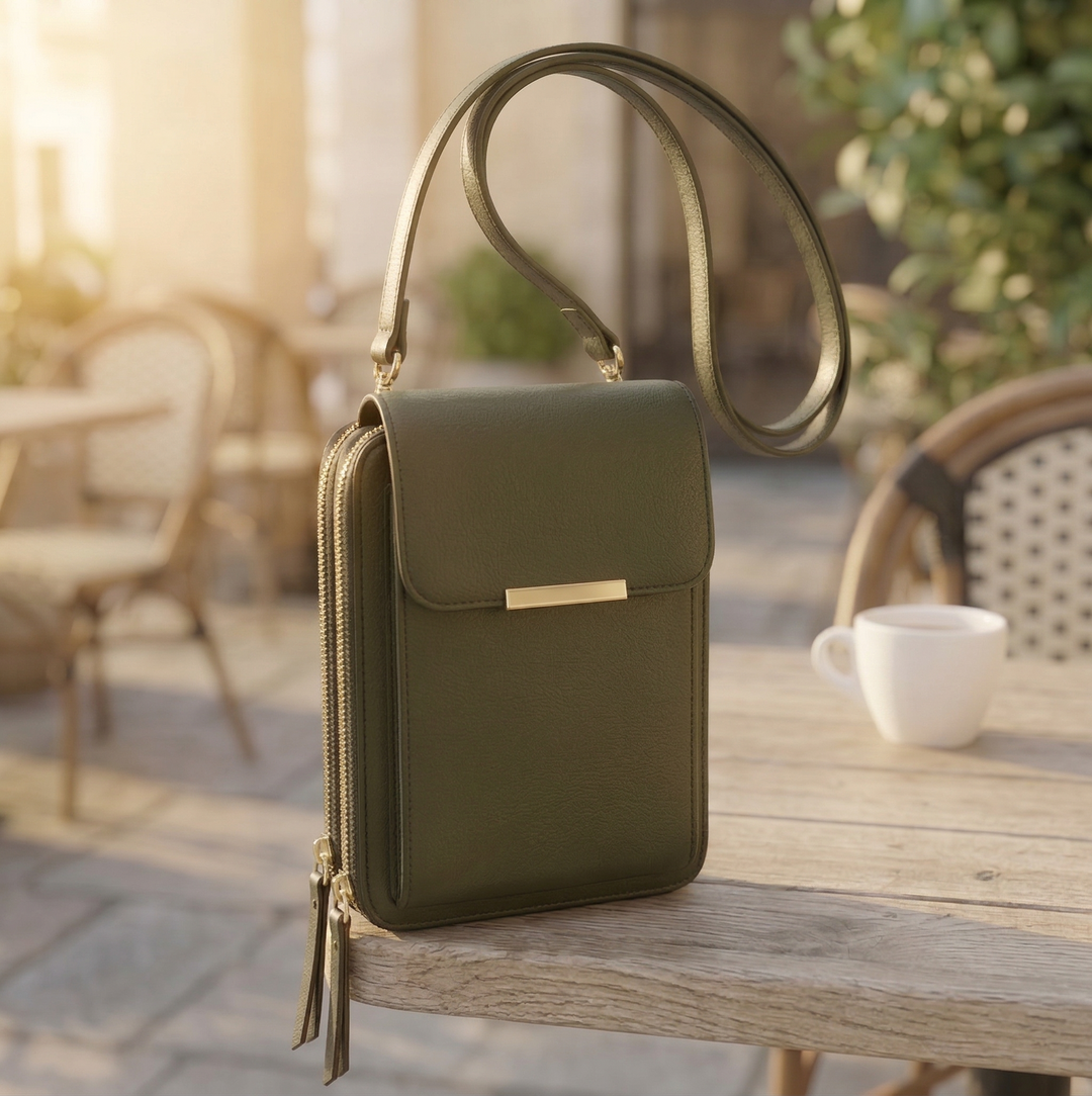 Crossbody-taske i mørk olivengrøn med guldfarvet spænde og tynd skulderrem, stående på et træbord ved en kaffekop. 5