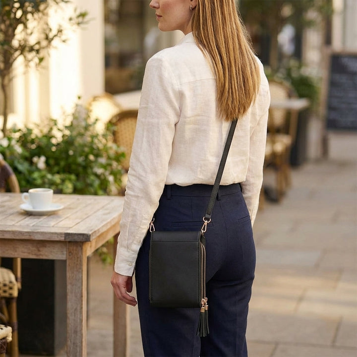 Kvinde set bagfra med sort crossbody-taske på hoften og rem over skulderen; baksiden af tasken er glat med lille kvast. 8