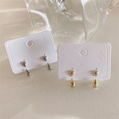 Zwei Paar Tropfen-Ohrringe, silber und gold, auf weißem Karton, elegantes Schmuckdesign.