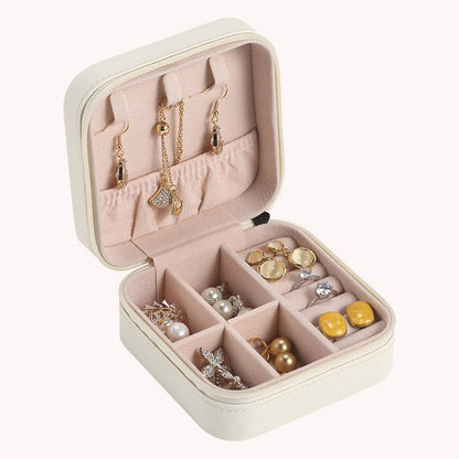 Beige Schmuckkästchen mit Ohrringen, Ringen und Halsketten, kompakt, ideal für Reisen.