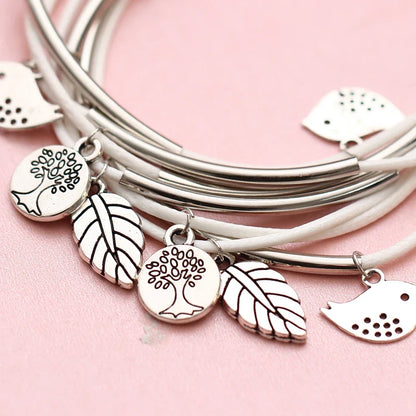 Silberne Armbänder mit Baum- und Blattanhängern auf rosa Hintergrund, Modeschmuck Accessoires.
