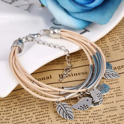 Beiges Lederarmband mit Vogel- und Blattanhängern, Damenmode, Schmuckaccessoire, Geschenkidee.