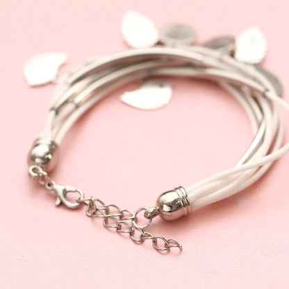 Mehrlagiges Armband aus weißem Leder mit silbernen Anhängern auf rosa Hintergrund.