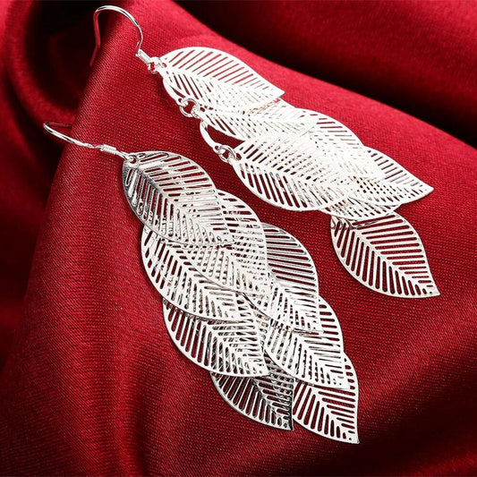 Silberne Blatt-Ohrringe auf rotem Stoff, filigranes Design, Modeschmuck, elegant und modern.