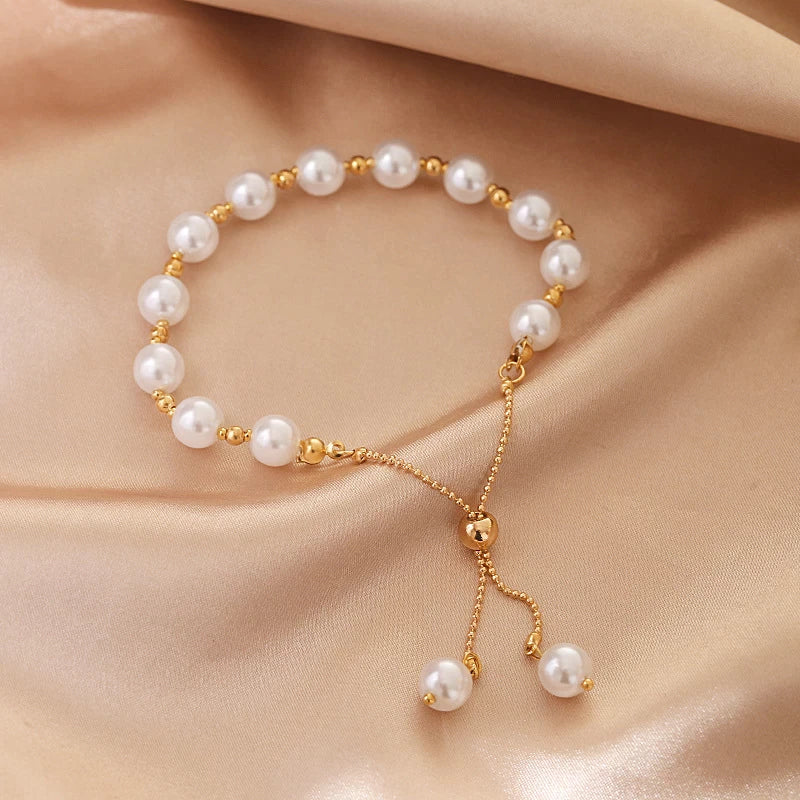 Goldenes Armband mit weißen Perlen auf beigem Stoff, eleganter Schmuck für Damen.