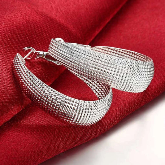 Silberne Creolen Ohrringe auf rotem Stoff, eleganter Schmuck, Damenaccessoire, Geschenkidee.