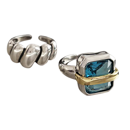 Zwei silberne Ringe, einer mit blauem Stein und goldener Fassung, der andere mit gewelltem Design.