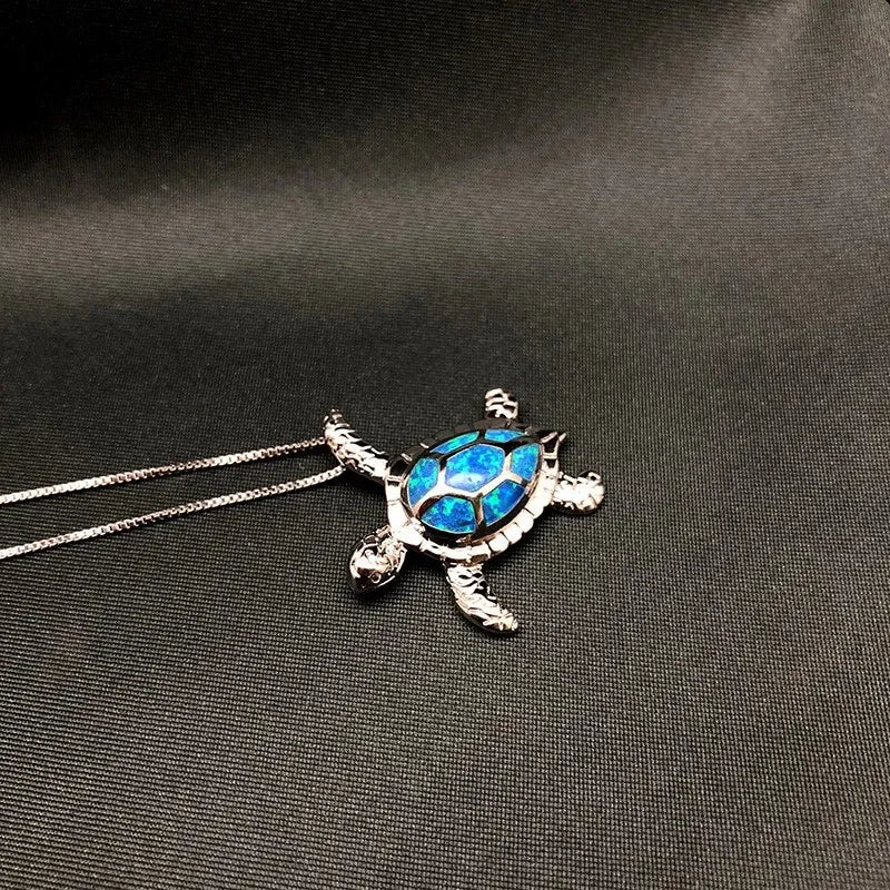 Silberne Schildkrötenkette mit blauem Opal-Anhänger auf schwarzem Hintergrund.