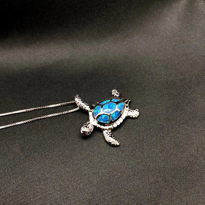 Silberne Schildkrötenkette mit blauem Opal-Anhänger auf schwarzem Hintergrund.