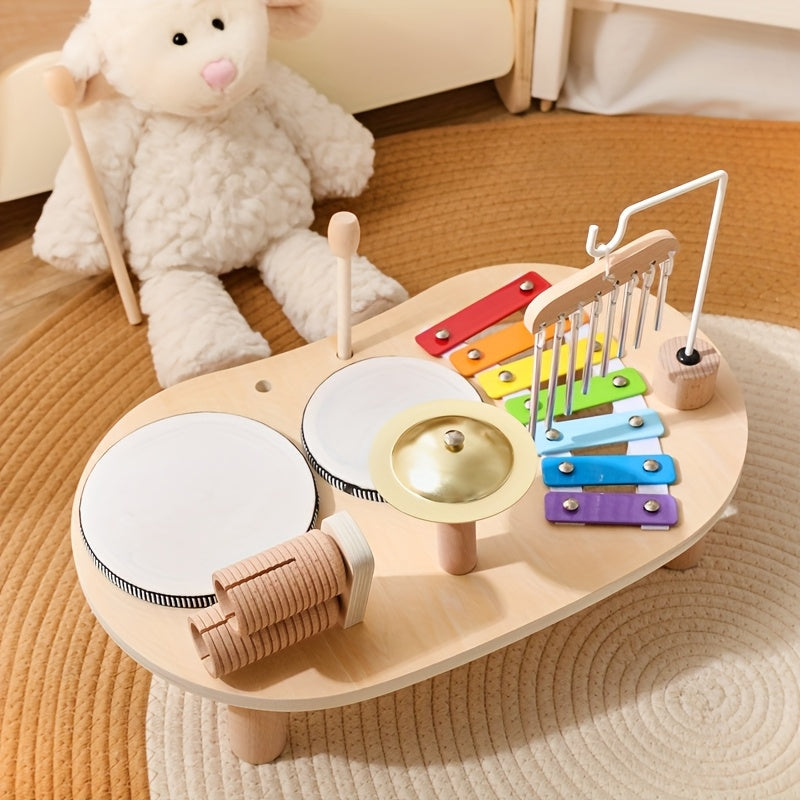 Musikbordet set fra den anden side med trommer og rasleruller i forgrunden og xylofonen med klokkespil bagest, ved siden af en hvid bamse. 4
