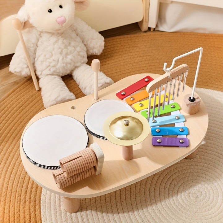 Musikbordet set fra den anden side med trommer og rasleruller i forgrunden og xylofonen med klokkespil bagest, ved siden af en hvid bamse. 4