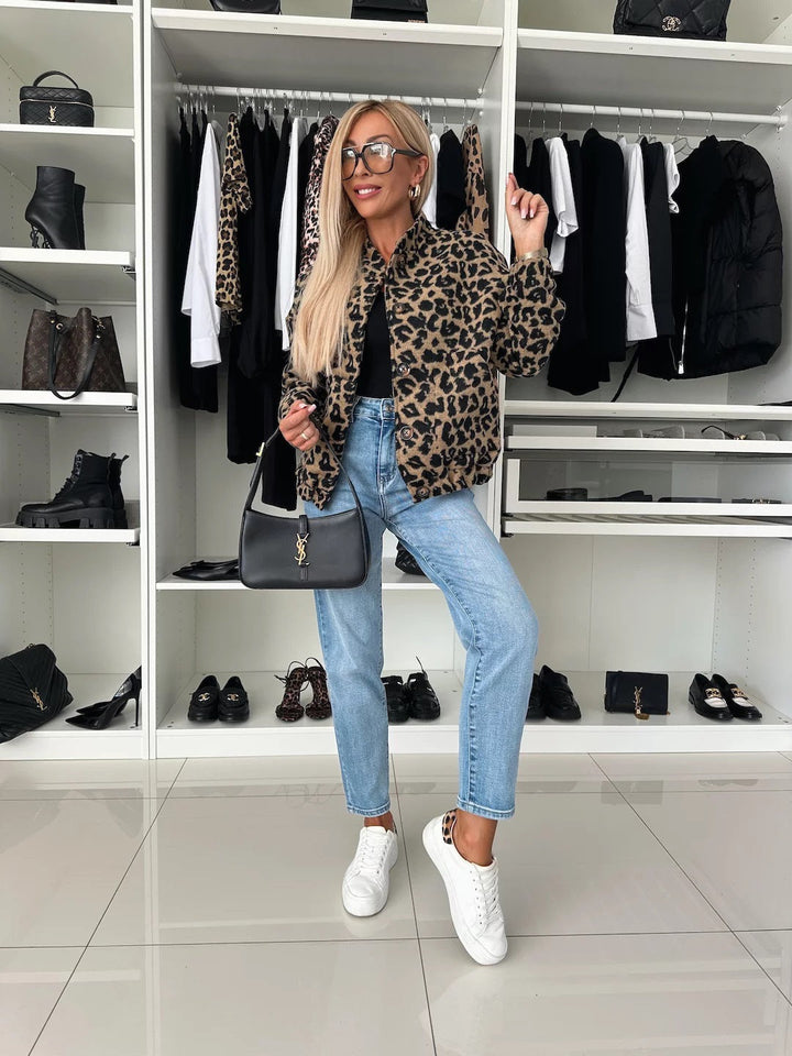 Helfigur af model i leopardbomberjakken med jeans, hvide sneakers og sort skuldertaske foran en åben garderobe med tøj og sko. 5