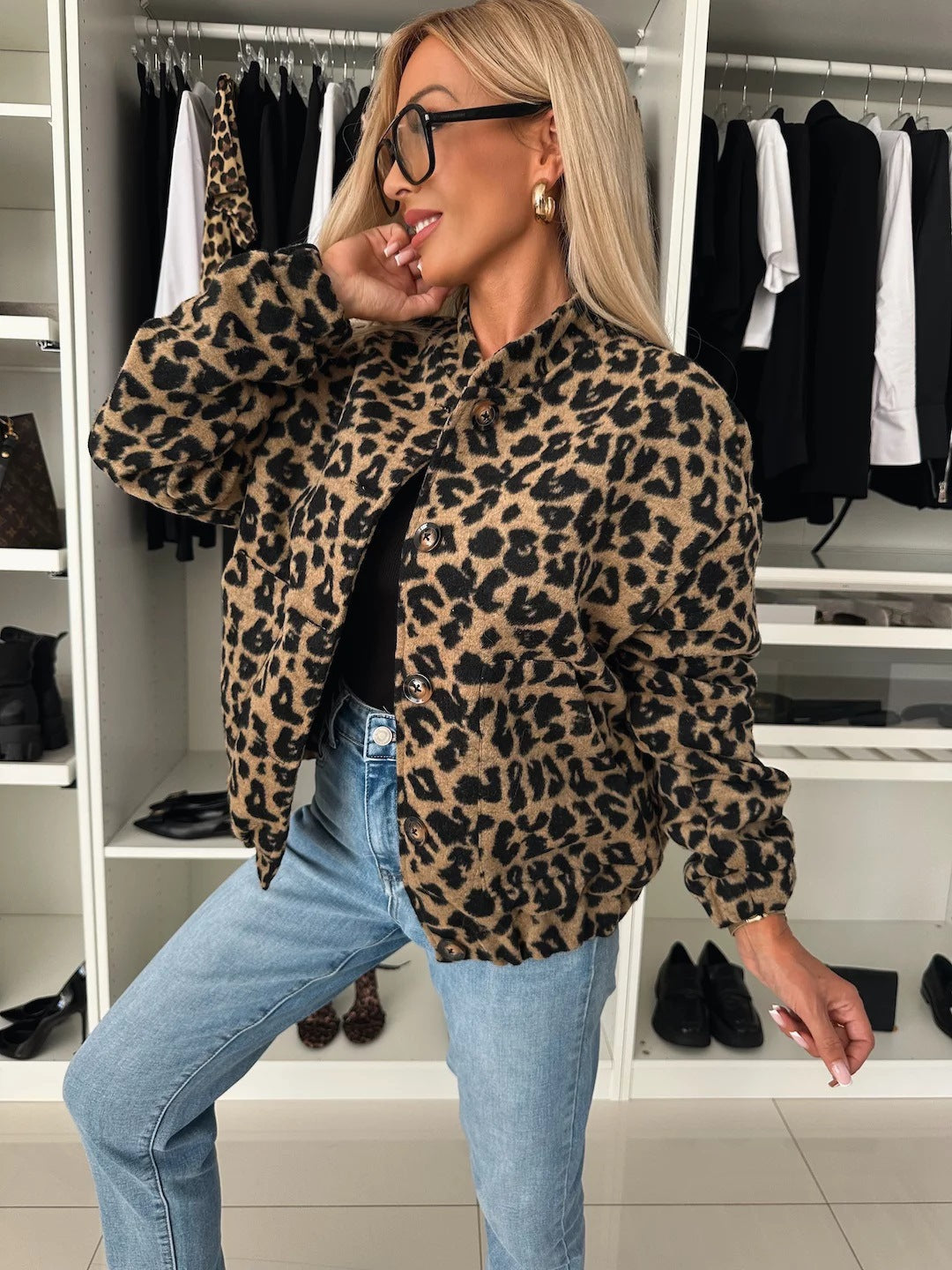 Model i leopardjakke med knapper og elastisk linning, båret åben over sort top og jeans, set på skrå foran i et garderoberum. 1