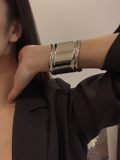 Silbernes, breites Metallarmband mit asymmetrischen Öffnungen, getragen am Handgelenk einer Frau.