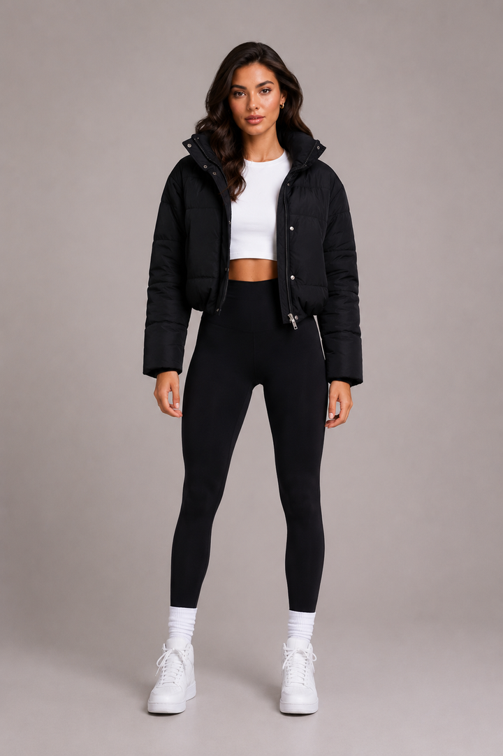 Model i fuld figur set forfra i kort sort quiltet jakke med høj krave, hvid top, sorte leggings og hvide sneakers. 2
