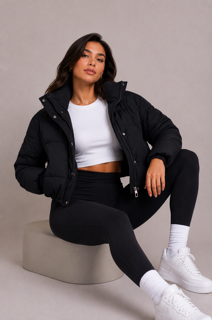 Siddende model på en grå blok, iført åben sort quiltet jakke med høj krave over hvid top og sorte leggings. 6