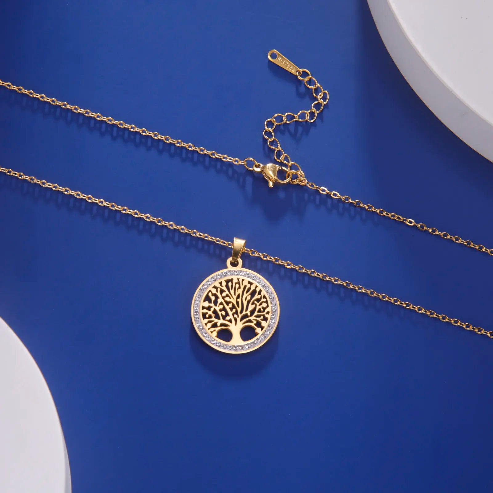 Goldene Halskette mit Lebensbaum-Anhänger auf blauem Hintergrund, eleganter Schmuck, Damenaccessoire.
