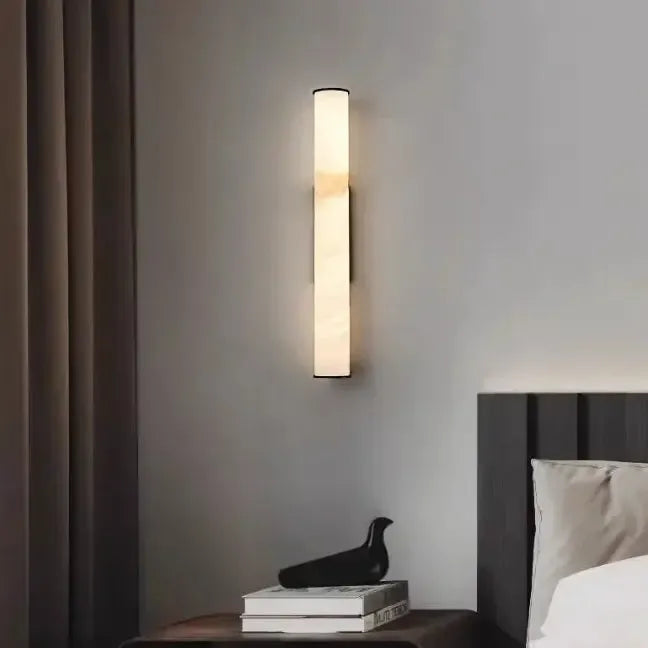 Tændt marmorlampe hænger over et natbord med bøger og en sort fuglefigur, ved siden af et gardin og en mørk sengegavl. 14