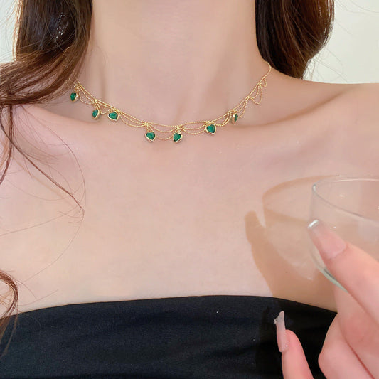 Frau mit goldener Halskette, grüne Edelsteine, elegantes Schmuckdesign, schwarzes Kleid.
