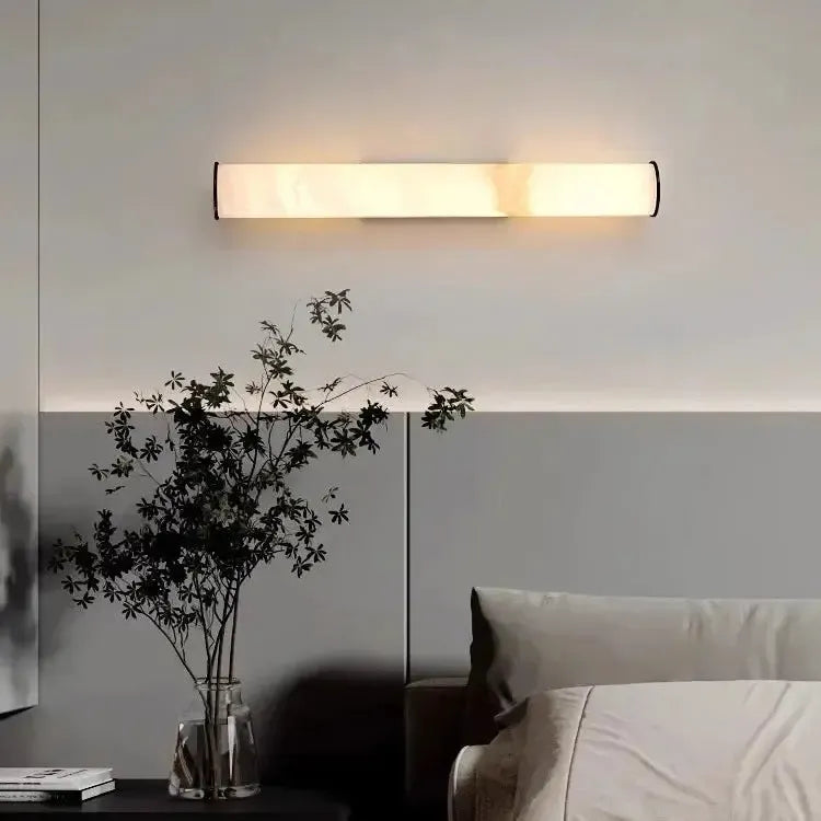 Marmorlampe monteret vandret på væggen over en seng, med en vase med sorte grene og bøger på et bord ved siden af. 16