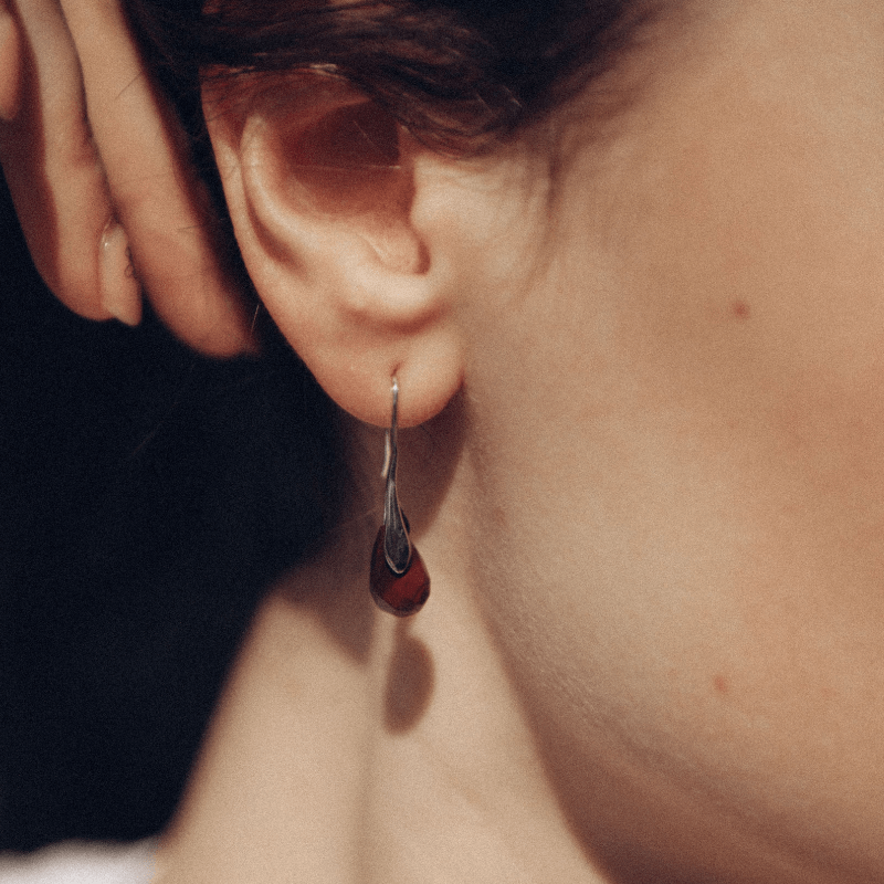 Frau mit silbernem Ohrring, Tropfenform, eleganter Schmuck, Nahaufnahme, stilvoll.