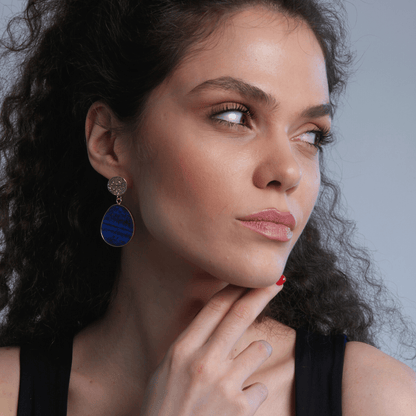 Frau mit blauen Ohrringen, lockigem Haar, schwarzem Top, nachdenklicher Blick.