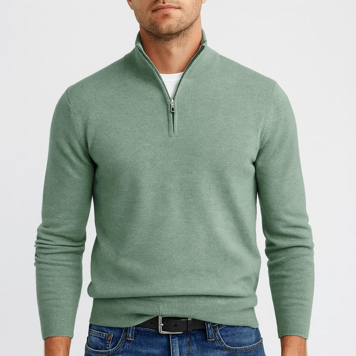 Model i grøn strikbluse med kort lynlås og høj krave, hvid t-shirt under og sort bælte. 12
