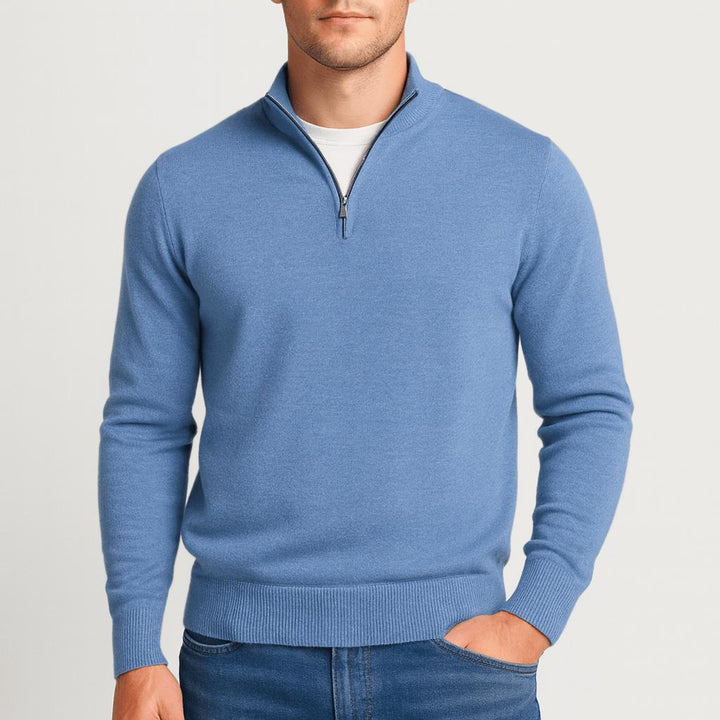 Model i blå strikbluse med lynlås i halsen, den ene hånd i jeanslommen, set forfra. 6