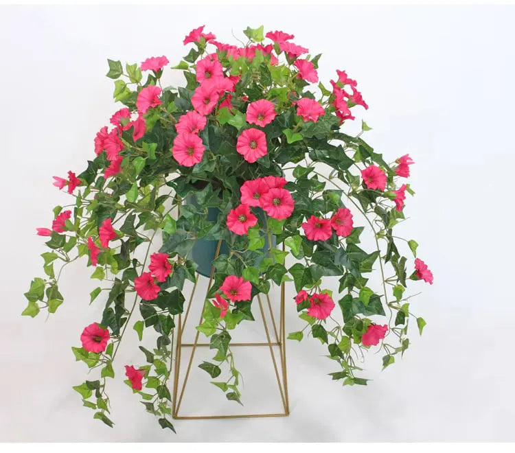 Pink kunstige blomster med nedhængende grønne blade i en blå urtepotte på et gyldent geometrisk stativ. 3