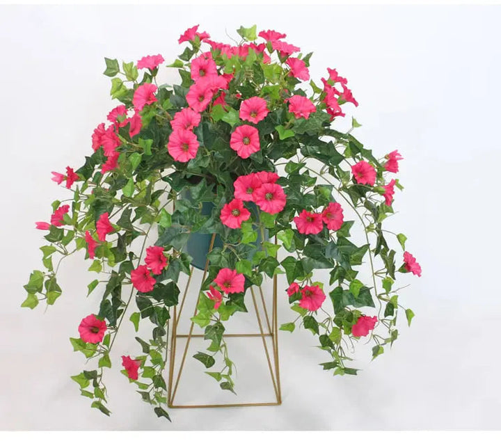 Pink kunstige blomster med nedhængende grønne blade i en blå urtepotte på et gyldent geometrisk stativ. 3