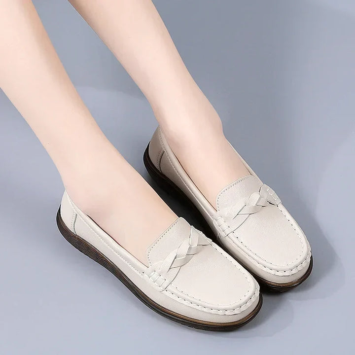 Beige loafers båret af model mod lysegrå baggrund, set skråt forfra med flettet pynt og mørk, tyk gummisål. 9