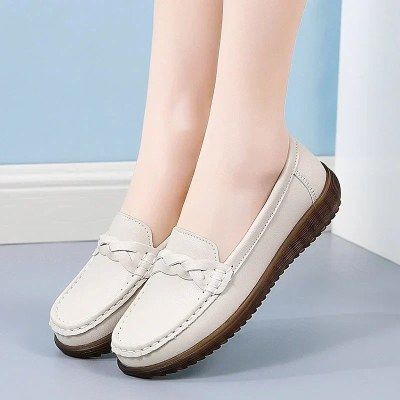 Beige loafers båret af model mod blå væg, set fra siden med flettet pynt og mørkebrun, ribbet sål. 10