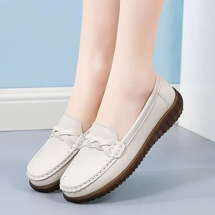 Beige loafers båret af model mod blå væg, set fra siden med flettet pynt og mørkebrun, ribbet sål. 10
