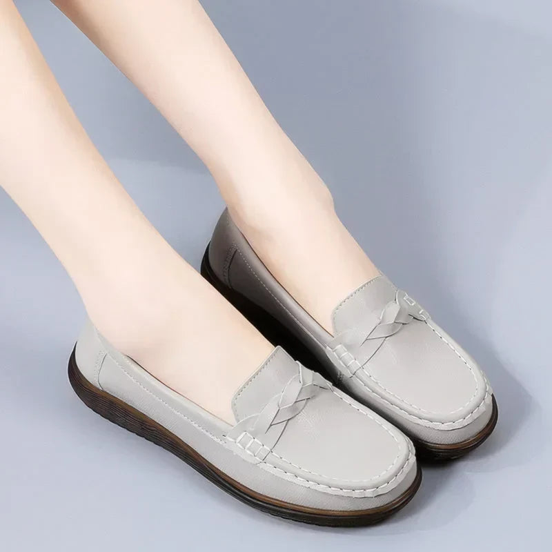 Lysegrå loafers båret af model mod grå baggrund, set skråt forfra med flettet pynt og mørk sål. 11