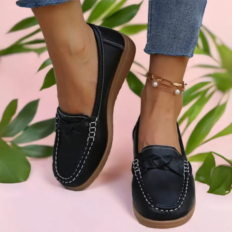 Sorte loafers båret af model mod lyserød baggrund med grønne blade, flettet detalje og hvid kontrastsyning på forskoen. 2