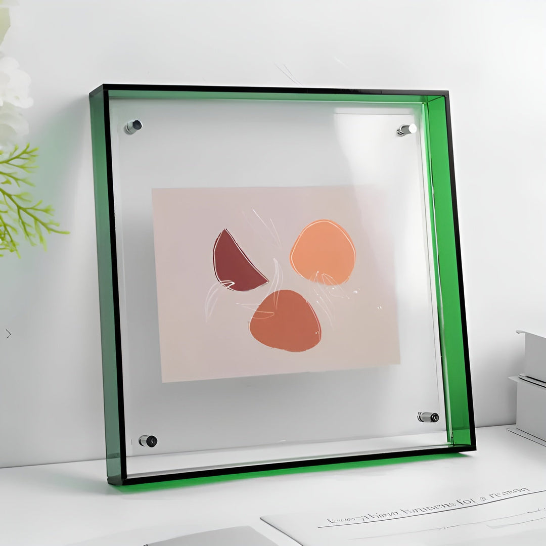 Firkantet akrylramme med grøn kant og synlige sølvfarvede fæstner, stillet på en hvid hylde med en abstrakt trykt illustration indeni. 21